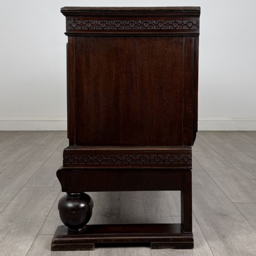 fig 3. A dark oak Edwardian low cupboard featuring three panelled doors, carved frieze borders, and turned bulbous legs on sledge feet.