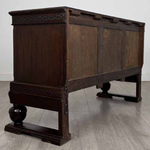 fig 4. A dark oak Edwardian low cupboard featuring three panelled doors, carved frieze borders, and turned bulbous legs on sledge feet.
