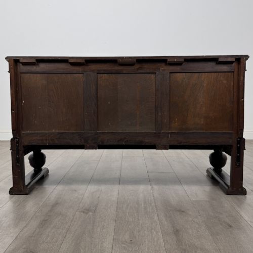fig 5. A dark oak Edwardian low cupboard featuring three panelled doors, carved frieze borders, and turned bulbous legs on sledge feet.