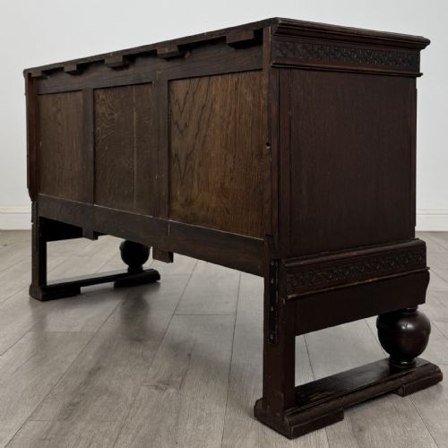 fig 6. A dark oak Edwardian low cupboard featuring three panelled doors, carved frieze borders, and turned bulbous legs on sledge feet.