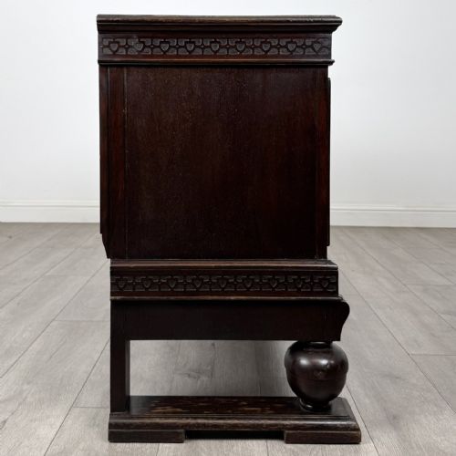fig 7. A dark oak Edwardian low cupboard featuring three panelled doors, carved frieze borders, and turned bulbous legs on sledge feet.