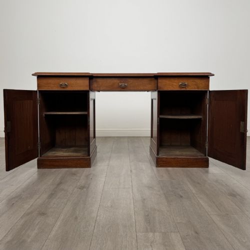 fig 1. A Victorian mahogany twin pedestal desk featuring a breakfront top, three upper frieze drawers, and two panelled cupboard doors on a plinth base.