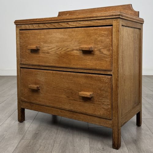 fig 1. An antique golden oak chest of drawers featuring two full-width drawers with matching rectangular wooden handles and a low raised gallery upstand.