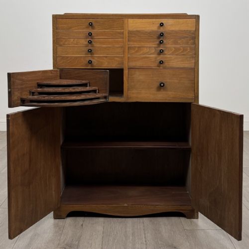 fig 1. An antique oak storage cabinet featuring multiple shallow drawers arranged above a double-door lower cupboard with small turned dark wooden knobs.