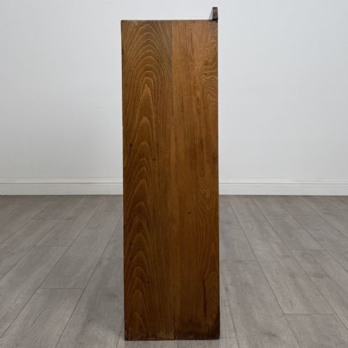 fig 3. An antique oak storage cabinet featuring multiple shallow drawers arranged above a double-door lower cupboard with small turned dark wooden knobs.