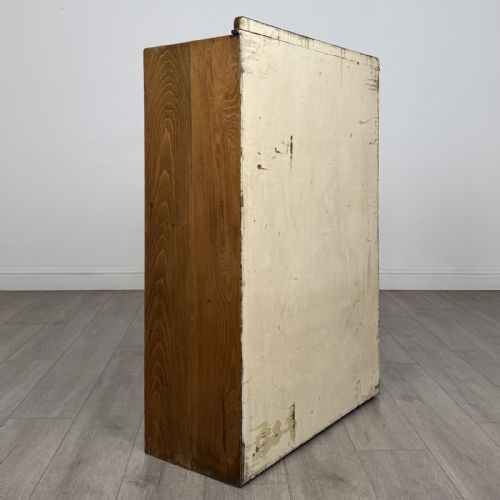 fig 4. An antique oak storage cabinet featuring multiple shallow drawers arranged above a double-door lower cupboard with small turned dark wooden knobs.