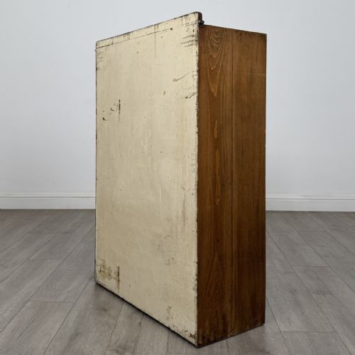 fig 6. An antique oak storage cabinet featuring multiple shallow drawers arranged above a double-door lower cupboard with small turned dark wooden knobs.
