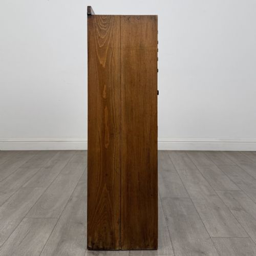 fig 7. An antique oak storage cabinet featuring multiple shallow drawers arranged above a double-door lower cupboard with small turned dark wooden knobs.
