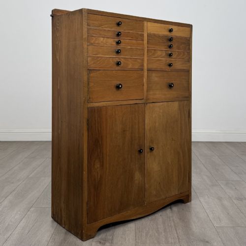 fig 8. An antique oak storage cabinet featuring multiple shallow drawers arranged above a double-door lower cupboard with small turned dark wooden knobs.
