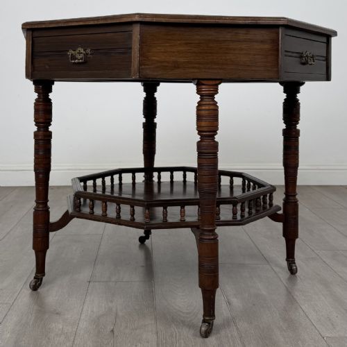 fig 1. An antique dark mahogany octagonal centre table featuring a drawer with a brass drop handle, ring-turned legs on brass castors, and an octagonal lower shelf with a spindle gallery.