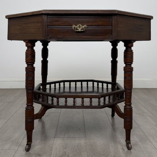 fig 2. An antique dark mahogany octagonal centre table featuring a drawer with a brass drop handle, ring-turned legs on brass castors, and an octagonal lower shelf with a spindle gallery.