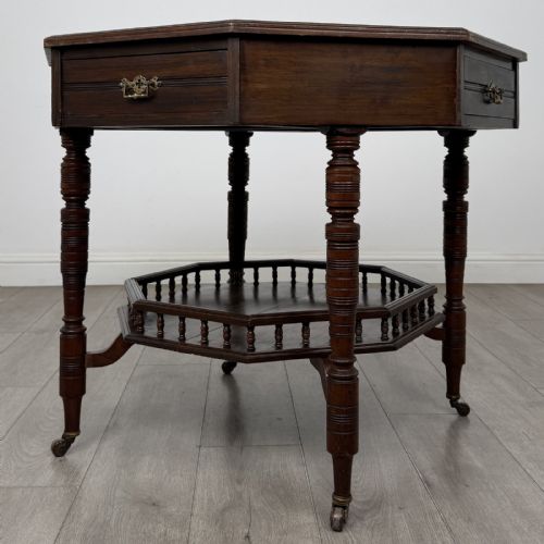 fig 3. An antique dark mahogany octagonal centre table featuring a drawer with a brass drop handle, ring-turned legs on brass castors, and an octagonal lower shelf with a spindle gallery.