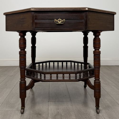 fig 4. An antique dark mahogany octagonal centre table featuring a drawer with a brass drop handle, ring-turned legs on brass castors, and an octagonal lower shelf with a spindle gallery.