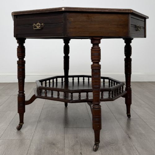 fig 5. An antique dark mahogany octagonal centre table featuring a drawer with a brass drop handle, ring-turned legs on brass castors, and an octagonal lower shelf with a spindle gallery.