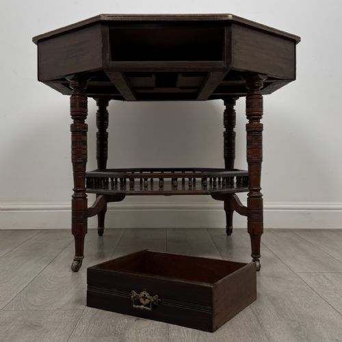 fig 7. An antique dark mahogany octagonal centre table featuring a drawer with a brass drop handle, ring-turned legs on brass castors, and an octagonal lower shelf with a spindle gallery.