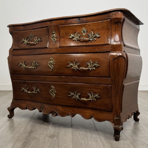 fig 1. An 18th-century French Louis XV bombe commode in warm brown cherrywood featuring ornate brass handles and cabriole legs.