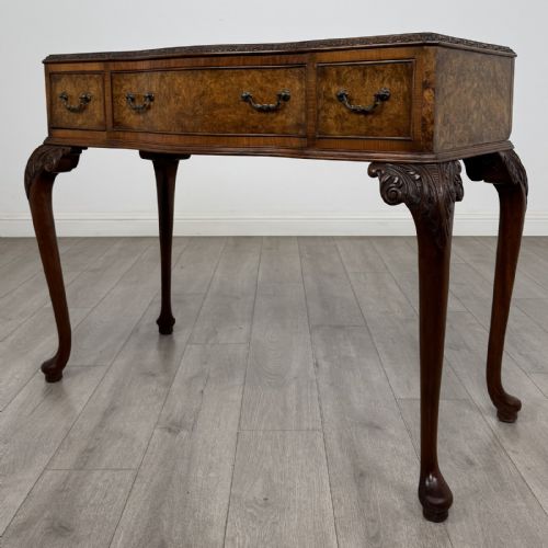 fig 1. An antique burr walnut writing table featuring three drawers, carved cabriole legs, and decorative brass handles.