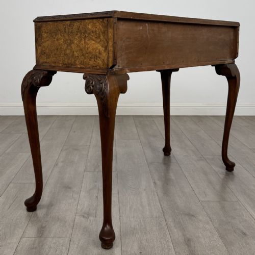 fig 3. An antique burr walnut writing table featuring three drawers, carved cabriole legs, and decorative brass handles.