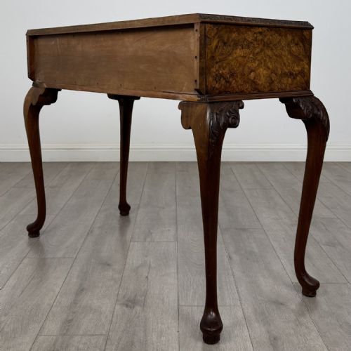 fig 5. An antique burr walnut writing table featuring three drawers, carved cabriole legs, and decorative brass handles.