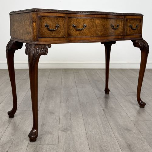 fig 7. An antique burr walnut writing table featuring three drawers, carved cabriole legs, and decorative brass handles.