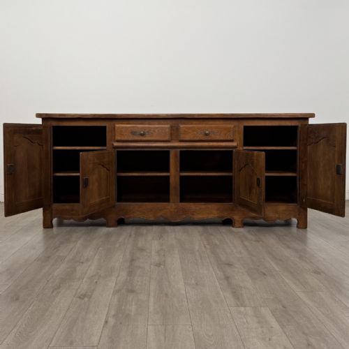 fig 1. A wide medium brown oak sideboard featuring four arched panel doors, two central drawers, decorative metal hardware, and a shaped apron.