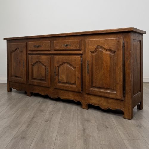 fig 2. A wide medium brown oak sideboard featuring four arched panel doors, two central drawers, decorative metal hardware, and a shaped apron.