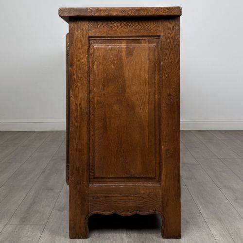 fig 3. A wide medium brown oak sideboard featuring four arched panel doors, two central drawers, decorative metal hardware, and a shaped apron.