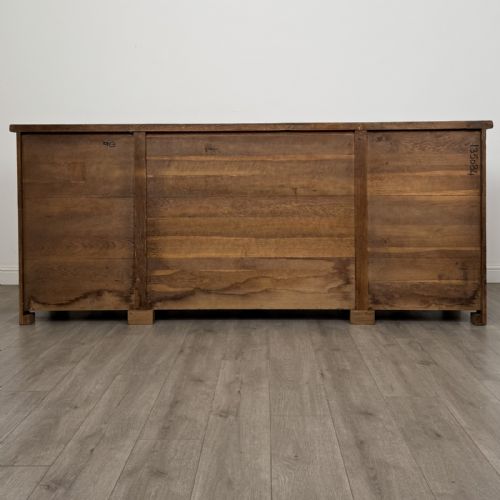 fig 5. A wide medium brown oak sideboard featuring four arched panel doors, two central drawers, decorative metal hardware, and a shaped apron.