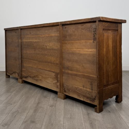 fig 6. A wide medium brown oak sideboard featuring four arched panel doors, two central drawers, decorative metal hardware, and a shaped apron.