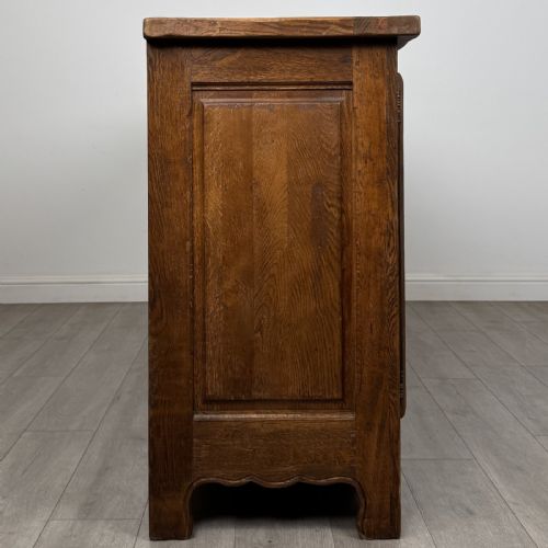 fig 7. A wide medium brown oak sideboard featuring four arched panel doors, two central drawers, decorative metal hardware, and a shaped apron.