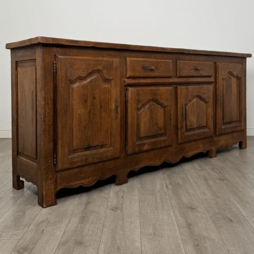 fig 8. A wide medium brown oak sideboard featuring four arched panel doors, two central drawers, decorative metal hardware, and a shaped apron.