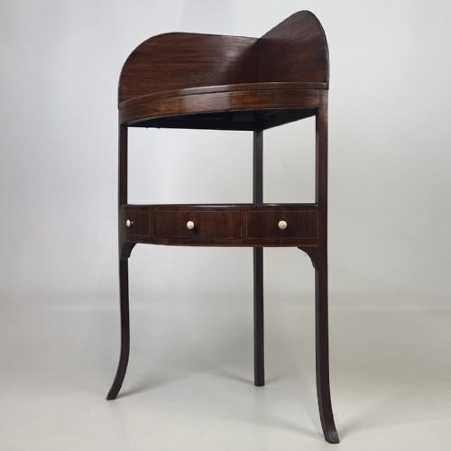 fig 1. A Georgian style mahogany corner stand featuring a curved raised gallery, inlaid drawer, white handles, and slender splayed legs.
