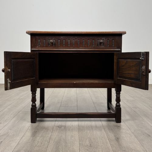 fig 1. A dark brown oak antique cupboard featuring a carved top drawer, panelled double doors with carved diamond motifs, and turned legs with stretchers.