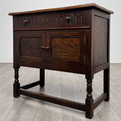 fig 2. A dark brown oak antique cupboard featuring a carved top drawer, panelled double doors with carved diamond motifs, and turned legs with stretchers.