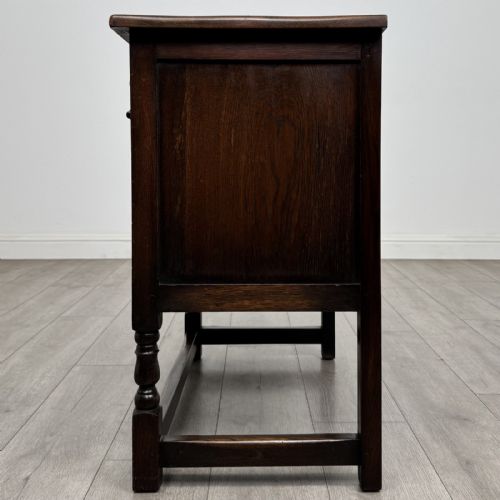 fig 3. A dark brown oak antique cupboard featuring a carved top drawer, panelled double doors with carved diamond motifs, and turned legs with stretchers.