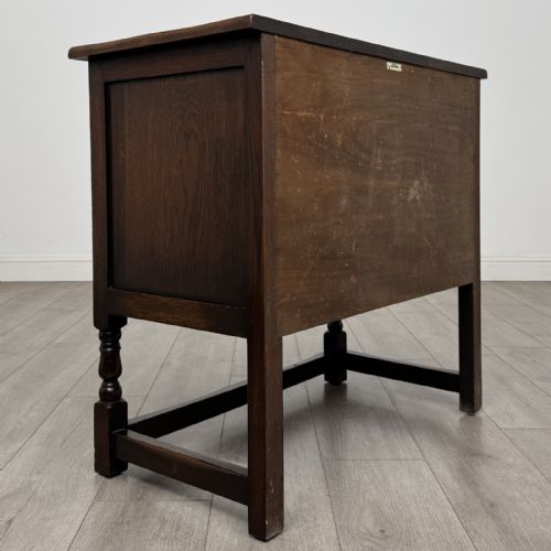 fig 4. A dark brown oak antique cupboard featuring a carved top drawer, panelled double doors with carved diamond motifs, and turned legs with stretchers.