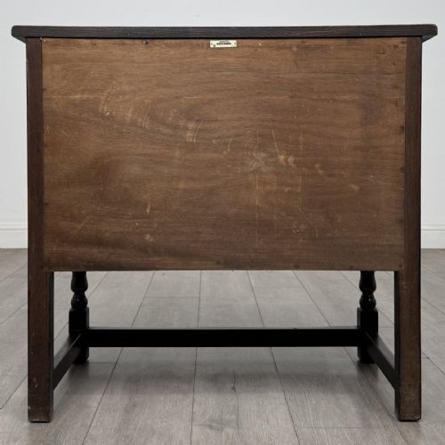 fig 5. A dark brown oak antique cupboard featuring a carved top drawer, panelled double doors with carved diamond motifs, and turned legs with stretchers.