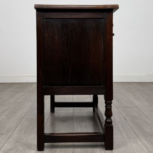 fig 7. A dark brown oak antique cupboard featuring a carved top drawer, panelled double doors with carved diamond motifs, and turned legs with stretchers.