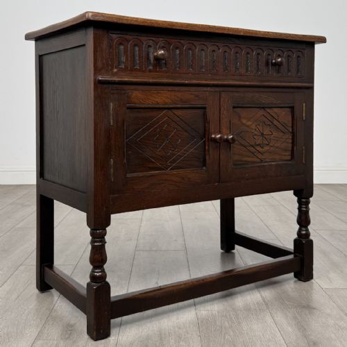 fig 8. A dark brown oak antique cupboard featuring a carved top drawer, panelled double doors with carved diamond motifs, and turned legs with stretchers.