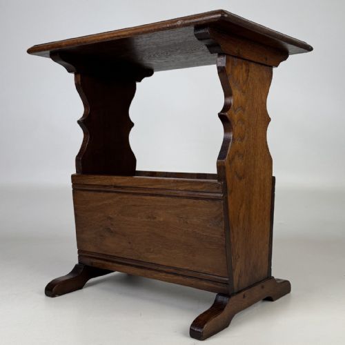 fig 1. A dark brown oak side table featuring a flat rectangular top supported by shaped vertical legs and a lower integrated magazine compartment.