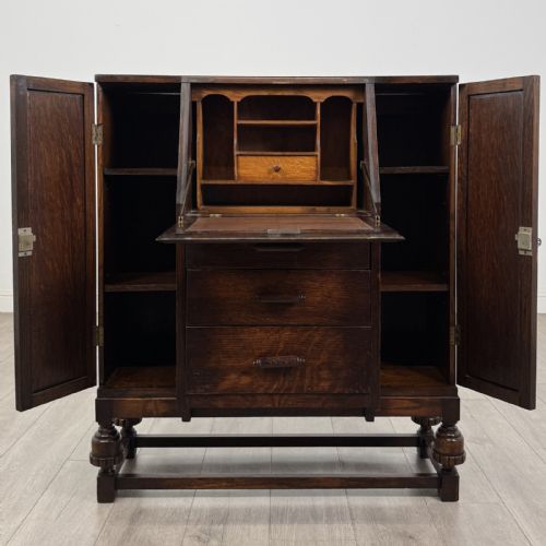 fig 1. A dark oak fitted bureau featuring a central slant-front writing slope over three drawers, flanked by two side cupboard doors and supported on turned feet with lower stretchers.