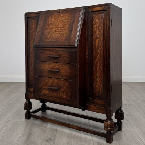 fig 2. A dark oak fitted bureau featuring a central slant-front writing slope over three drawers, flanked by two side cupboard doors and supported on turned feet with lower stretchers.