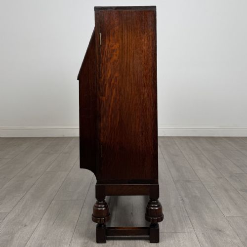 fig 3. A dark oak fitted bureau featuring a central slant-front writing slope over three drawers, flanked by two side cupboard doors and supported on turned feet with lower stretchers.