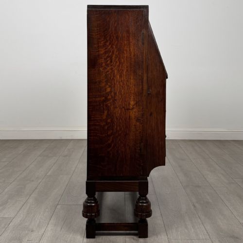 fig 7. A dark oak fitted bureau featuring a central slant-front writing slope over three drawers, flanked by two side cupboard doors and supported on turned feet with lower stretchers.