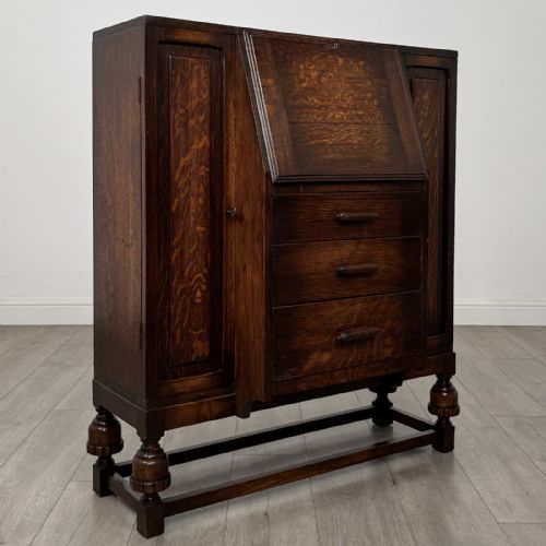 fig 8. A dark oak fitted bureau featuring a central slant-front writing slope over three drawers, flanked by two side cupboard doors and supported on turned feet with lower stretchers.