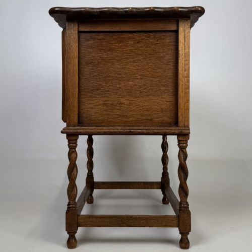fig 3. An Edwardian oak side cabinet featuring a single panelled door, a scalloped edge top, and four barley twist legs joined by a lower stretcher.