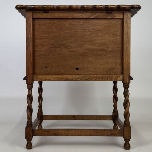 fig 5. An Edwardian oak side cabinet featuring a single panelled door, a scalloped edge top, and four barley twist legs joined by a lower stretcher.