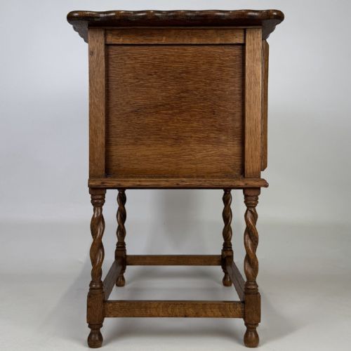 fig 7. An Edwardian oak side cabinet featuring a single panelled door, a scalloped edge top, and four barley twist legs joined by a lower stretcher.