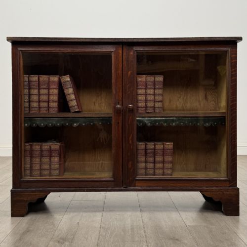 fig 1. A low Victorian dark oak display cabinet featuring two glazed doors, turned wooden knobs, bracket feet, and a single interior shelf trimmed with scalloped leather.