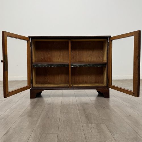 fig 2. A low Victorian dark oak display cabinet featuring two glazed doors, turned wooden knobs, bracket feet, and a single interior shelf trimmed with scalloped leather.